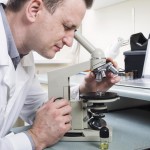 male-in-white-lab-coat-looking-into-microscope